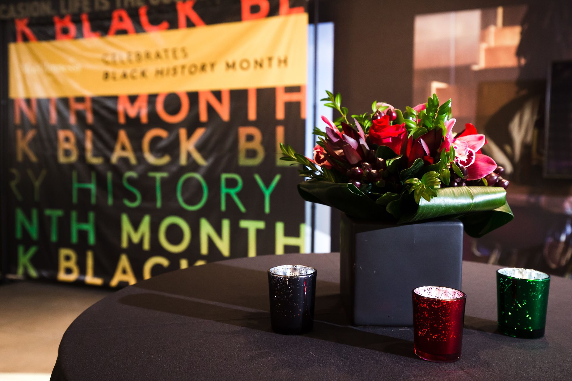 Flowers on a table in front of a step and repeat that says "Black History Month"